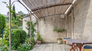 Eine überdachte Terrasse mit Tisch und Stühlen, umgeben von Blumentöpfen und einer Betonmauer.