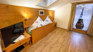 Quarto de madeira com uma cama, uma televisão e uma janela com cortinas.
