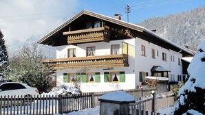 Un edificio de dos pisos con un balcón, cerca viva de madera y alrededores cubiertos de nieve.