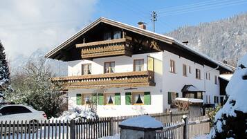 Ein zweistöckiges Gebäude mit Balkon, Holzzaun und verschneiter Umgebung.