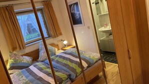 Un dormitorio acogedor con una cama de madera, una mesita de noche con lámpara, una ventana con cortinas y un baño visible a través de una puerta abierta.