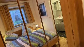 Ein gemütliches Schlafzimmer mit einem hölzernen Bett, einem Nachttisch mit Lampe, einem Fenster mit Vorhängen und einem durch eine offene Tür einsehbaren Badezimmer.