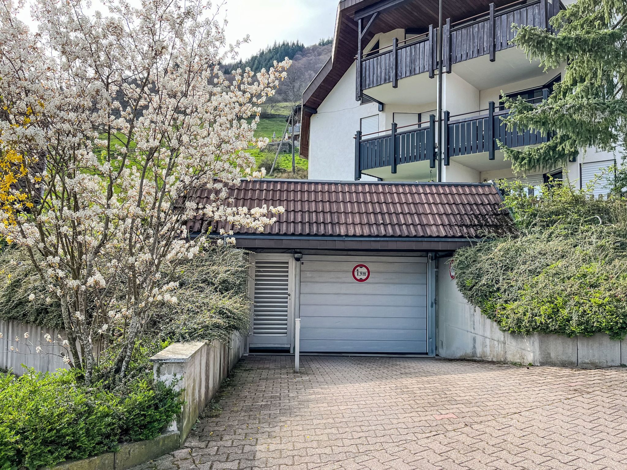 A building with a garage door, a balcony, and a tree with white blossoms.
