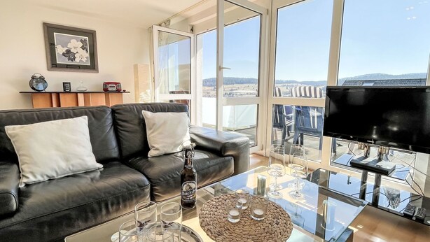 Una sala de estar moderna con un sofá de cuero negro, una mesa de centro de vidrio y un amplio ventanal con vistas a la ciudad.