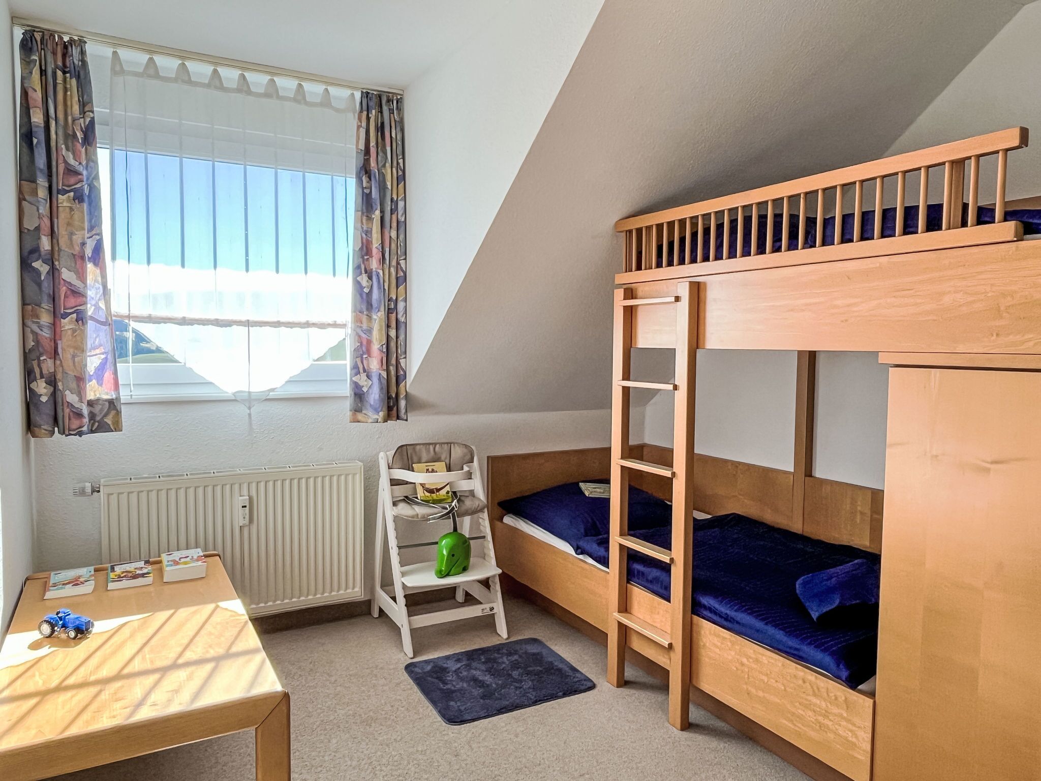 A room with a bunk bed, a small desk, a chair, and a radiator.