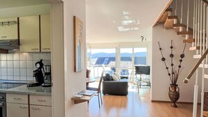 Una cocina moderna con cafetera, un comedor con mesa y sillas, un sofá y una escalera con un jarrón decorativo.
