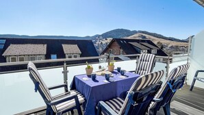 Un balcón con una mesa preparada para dos personas, con vistas a un paisaje de casas y colinas.