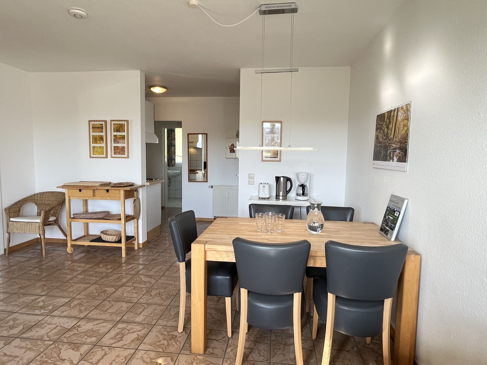 Un coin repas avec une table et des chaises en bois, un espace cuisine avec un évier et des placards, et un couloir menant à une salle de bain.