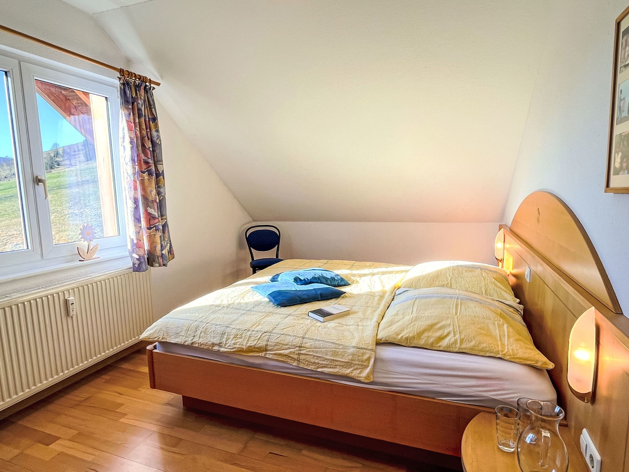 A bedroom with a wooden bed, a chair, a radiator, and a window with curtains.