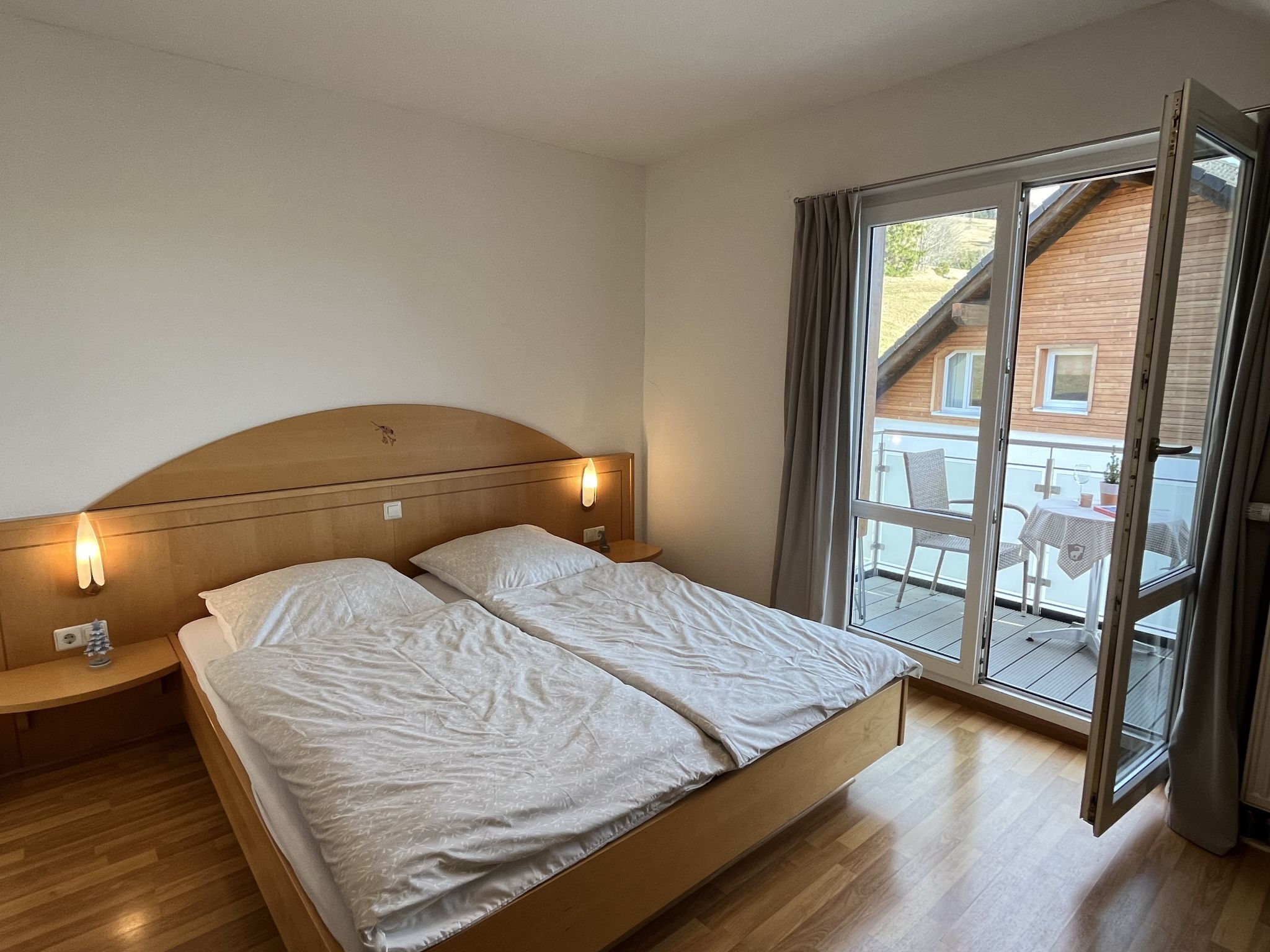 A bedroom with a wooden bed, two bedside tables, and a large sliding glass door leading to an outdoor balcony.