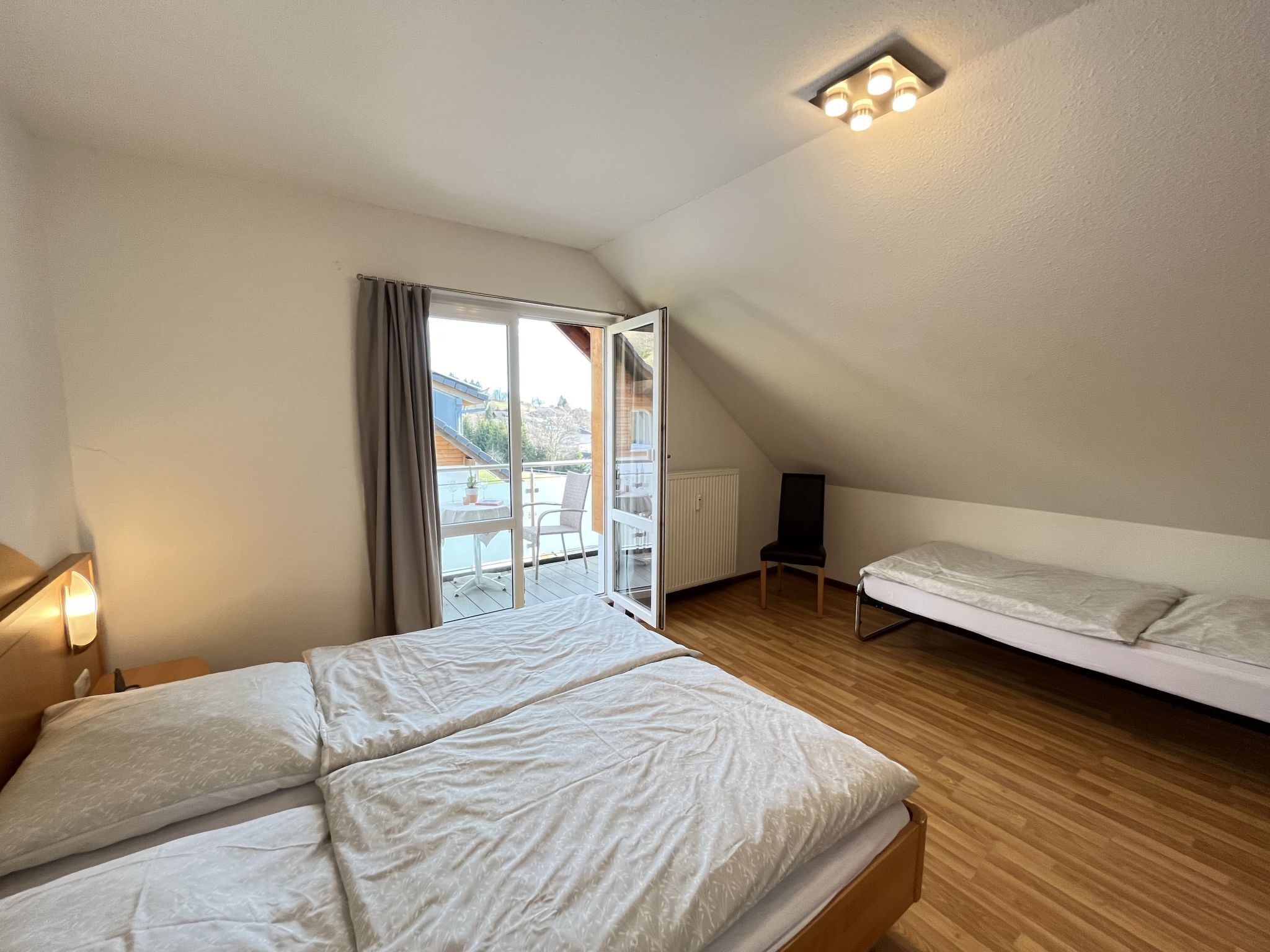 A bedroom with a bed, a chair, a small table, and a window with curtains.
