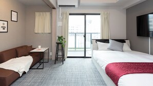 Ein Hotelzimmer mit einem braunen Sofa, einem Bett mit roter Decke, einem kleinen Tisch mit Pflanze und einem Fernseher an der Wand.