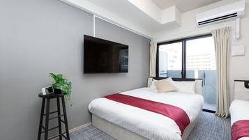 A hotel room with a bed, a TV mounted on the wall, a small table with a plant, and a window with curtains.