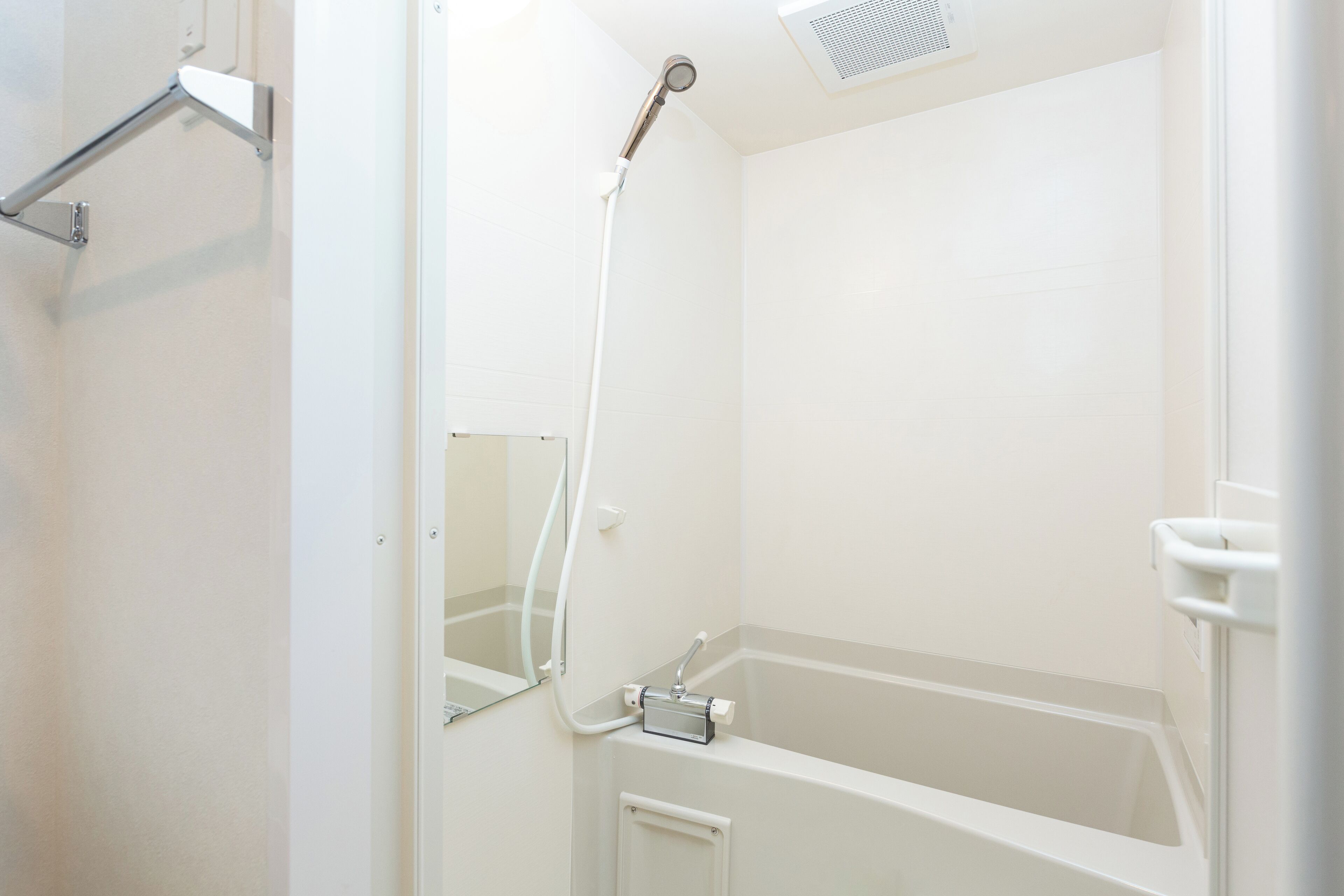 Une salle de bain blanche avec une douche, un miroir et des toilettes.