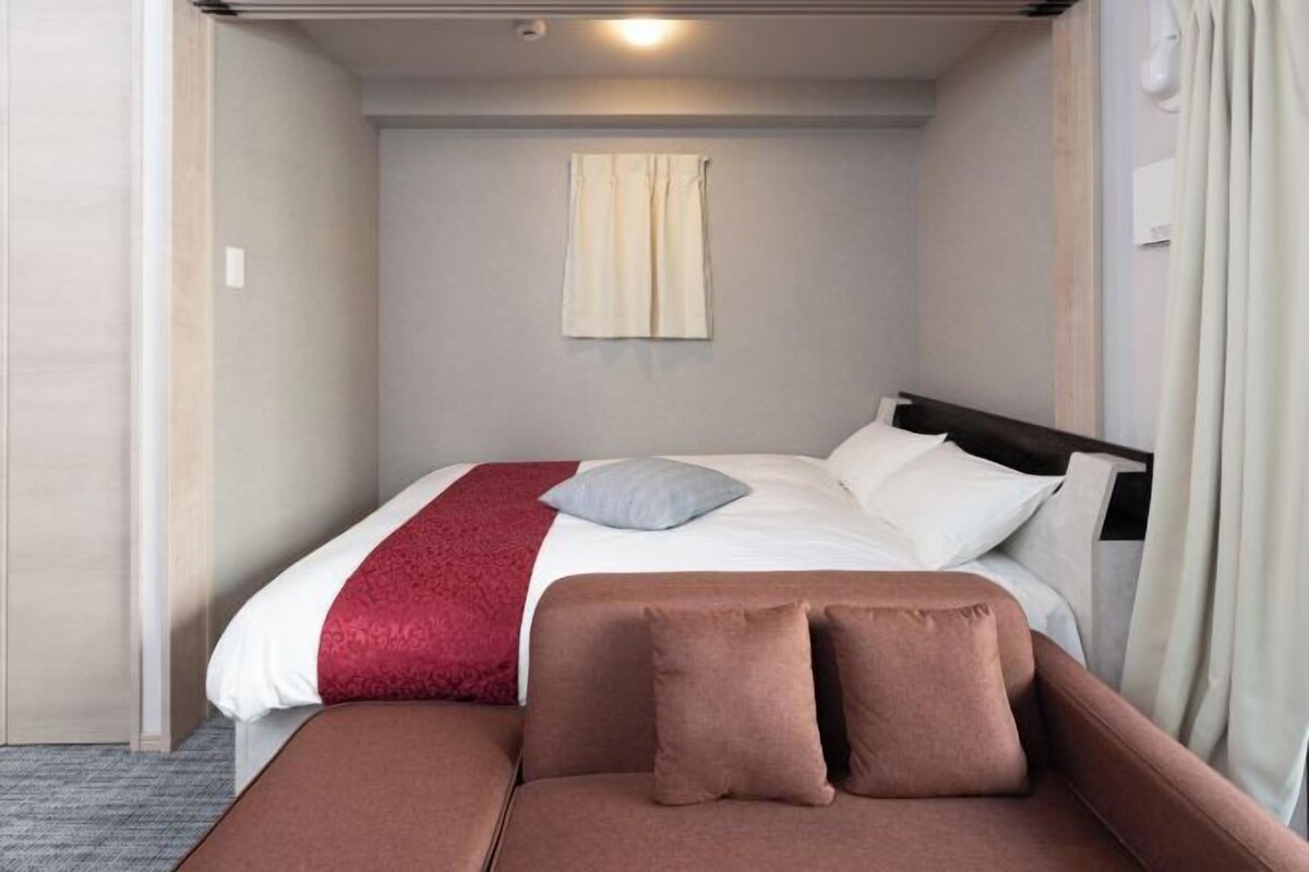 Ein Hotelzimmer mit Bett, einer Couch, einem Fenster mit Vorhängen und einer Deckenleuchte.