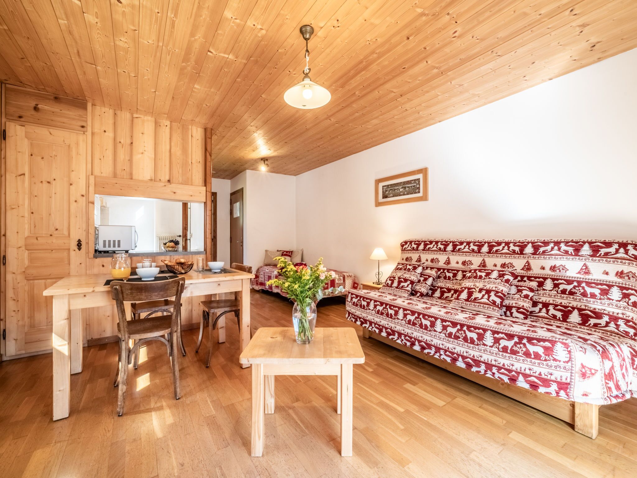 A wooden interior with a dining table, chairs, a sofa, and a small table with a vase.