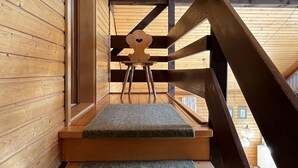 A wooden staircase with a cushioned landing, leading to a room with a wooden ceiling and a window.