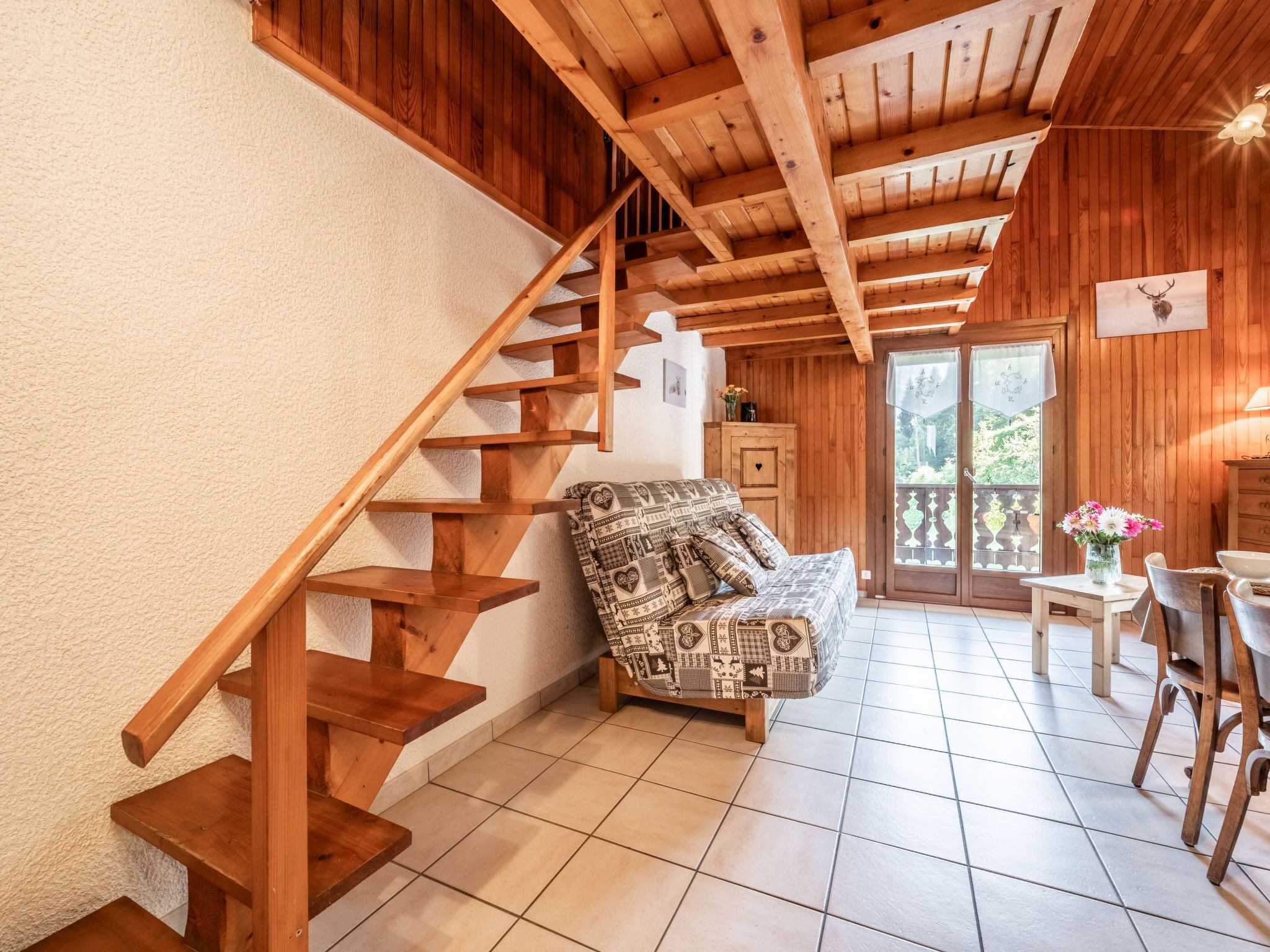 A wooden staircase leading to a balcony, a patterned sofa, and a dining area with a table and chairs.
