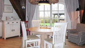 Ein rustikaler Essbereich mit einem Holztisch, weißen Stühlen, einer weißen Kommode mit Schubladen und einem karierten Sofa.