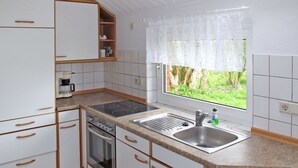A compact kitchen with white cabinets, a built-in oven, a stove, a sink, and a window with a view of greenery.
