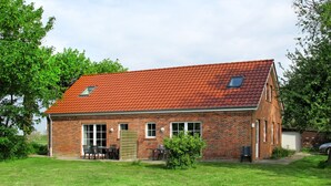 A single-story brick house with a red-tiled roof, a small attached garage, and a front yard with a lawn and a few trees.