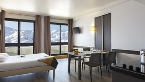 Ein Hotelzimmer mit Bett, Esstisch mit Stühlen, Fernseher und Blick auf schneebedeckte Berge.