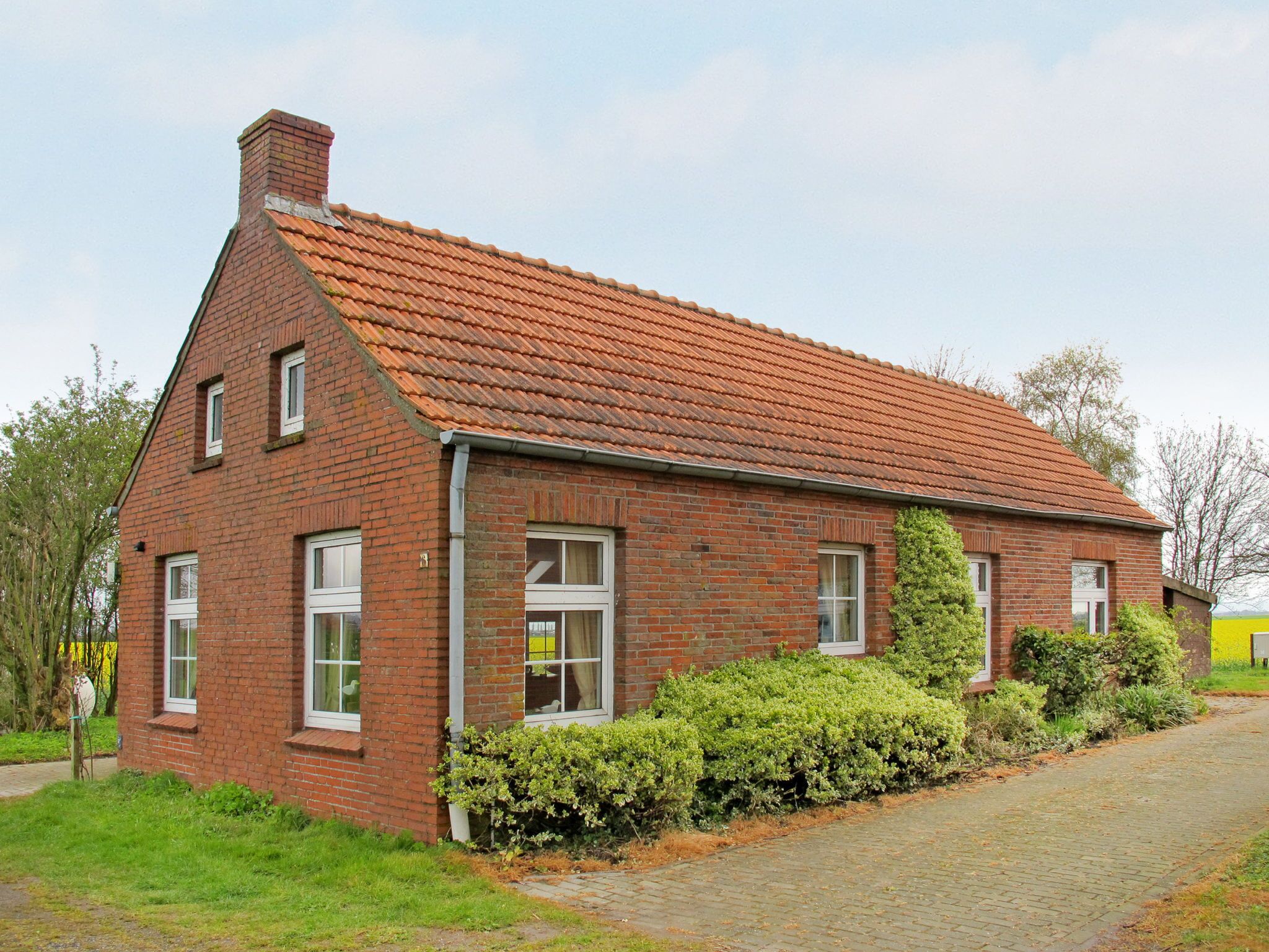 A two-story brick house with a red-tiled roof, a chimney, and a paved driveway.