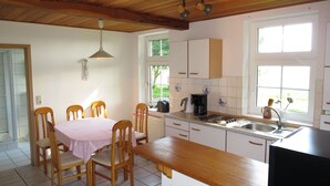Une cuisine avec des meubles de rangement en bois, une table à manger avec des chaises, une machine à café et un four à micro-ondes.