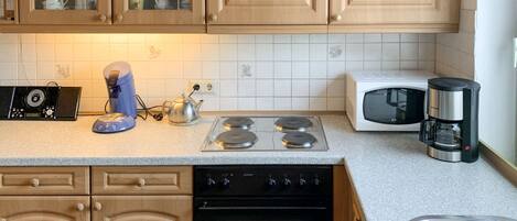 Una cocina con armarios de madera, estufa, microondas, cafetera y hervidor.