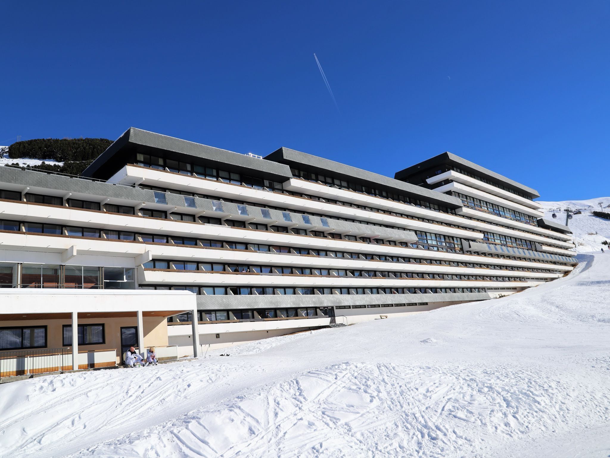 Un hôtel moderne à plusieurs étages, doté de grandes fenêtres et offrant une vue sur une piste de ski en arrière-plan.