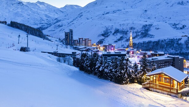 A snow-covered mountain town with a prominent church tower, ski slopes, and modern buildings.