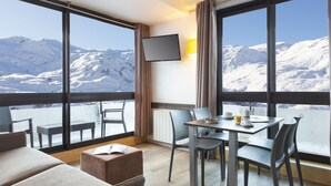 A hotel room with a balcony, a dining table, and a TV mounted on the wall.