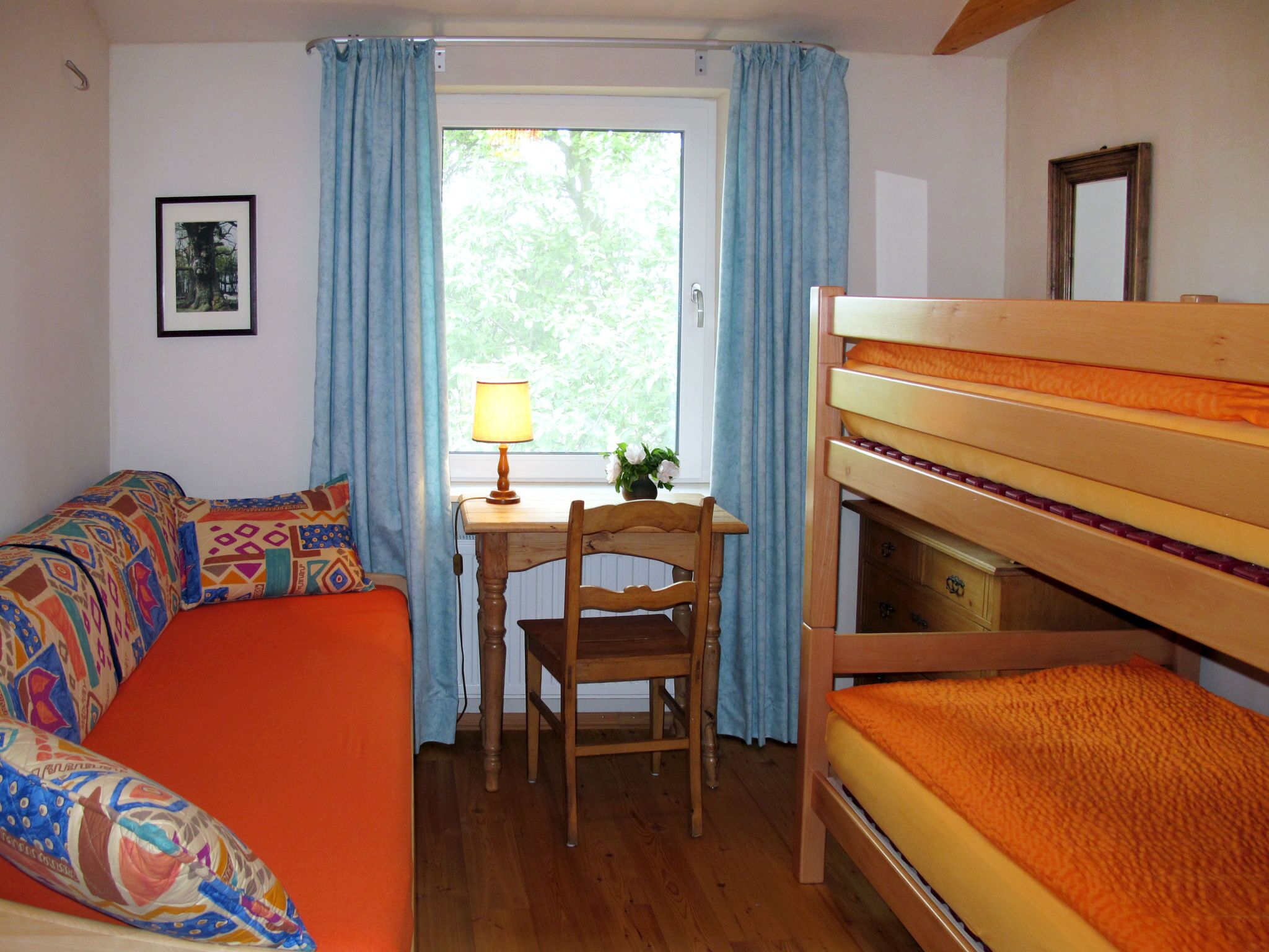 Une chambre avec un lit superposé, un bureau avec une lampe, une chaise et une fenêtre avec des rideaux.