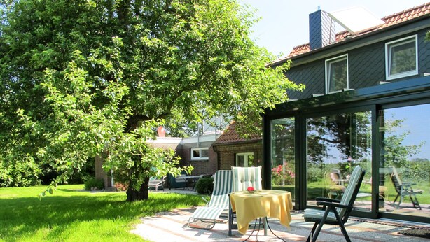 A patio with outdoor furniture, a table with a yellow tablecloth, and a large glass door leading to a garden. - Landhaus Mahnhamm by Interhome (Horumersiel)