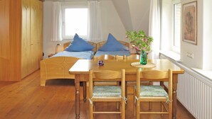 A cozy room with a wooden bed, a dining table with chairs, and a vase with flowers. - Landhaus Mahnhamm by Interhome (Horumersiel)