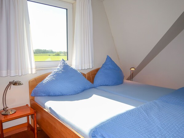 A bedroom with a bed, a nightstand, a lamp, and a window with curtains. - Landhaus Mahnhamm by Interhome (Horumersiel)