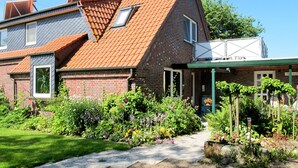 A two-story house with a sloped roof, brick exterior, and a garden with various plants and flowers. - Landhaus Mahnhamm by Interhome (Horumersiel)