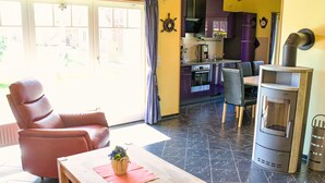 A living room with a sofa, a wooden table, and a potted plant. There is a kitchen in the background with a stove and cabinets. - Klipper by Interhome (Burhave)