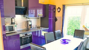 A modern kitchen with purple cabinets, a microwave, stove, and a dining area with a table and chairs. - Klipper by Interhome (Burhave)