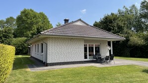 A single-story house with a tiled roof, a covered patio with outdoor furniture, and a well-maintained lawn. - Klipper by Interhome (Burhave)