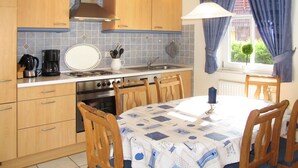 Une cuisine avec des meubles de rangement en bois, une cuisinière, un évier et une table à manger avec des chaises.
