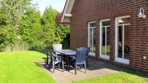 Une terrasse avec une table et des chaises, un bâtiment en briques et une pelouse verdoyante.
