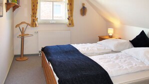 Une chambre avec deux lits, un radiateur, une fenêtre avec des rideaux, une table de chevet avec une lampe et une étagère avec des livres.