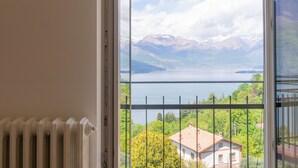 A room with a view of a lake, mountains, and a house across the water. - Apartment Alloro by Interhome (Varenna)