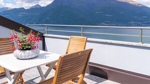 A balcony with a table and chairs, a wicker basket with flowers, and a view of mountains and a lake. - Apartment Alloro by Interhome (Varenna)