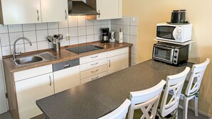 A modern kitchen with white cabinets, a granite countertop, a built-in stove, a sink, and a microwave. There are two white chairs at the counter. - Tossens by Interhome (Tossens)
