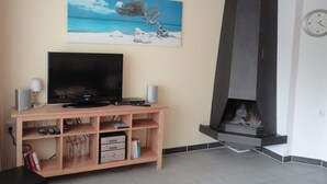 A living room with a flat-screen TV on a wooden stand, a fireplace, and a painting of a beach scene on the wall. - Tossens by Interhome (Tossens)