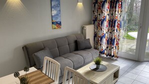 Een moderne woonkamer met een grijze bank, witte stoelen, een houten salontafel en een kleine potplant.