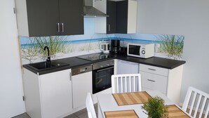 Een kleine keuken met witte kastjes, een zwart aanrecht, een magnetron, een koffiezetapparaat en een spoelbak.