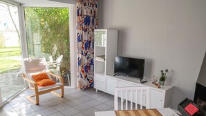Een moderne woonkamer met een witte bank, een televisie en een eethoek met een tafel en stoelen.